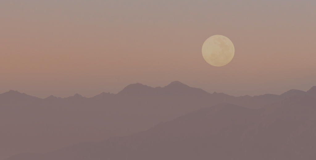 a pink sunset over mountains with a full moon