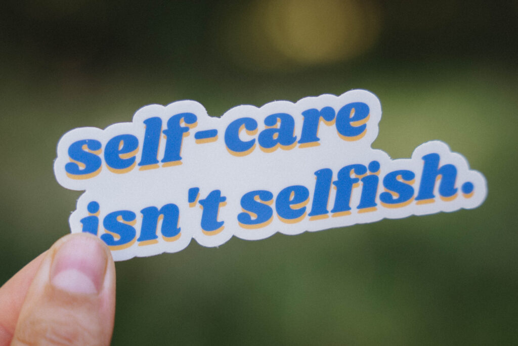 Spotlighting our Sticker Collection! Sticker that says "self-care isn't selfish" held up in front of a green background