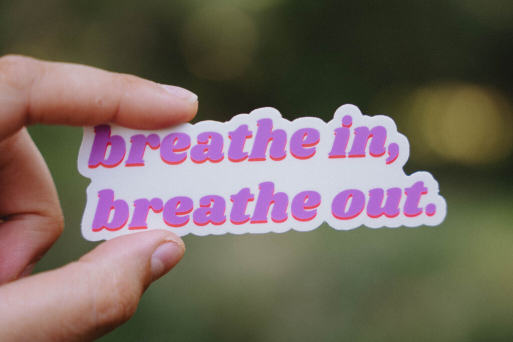 Spotlighting our Sticker Collection! Sticker that says "breathe in, breathe out" held up in front of a green background