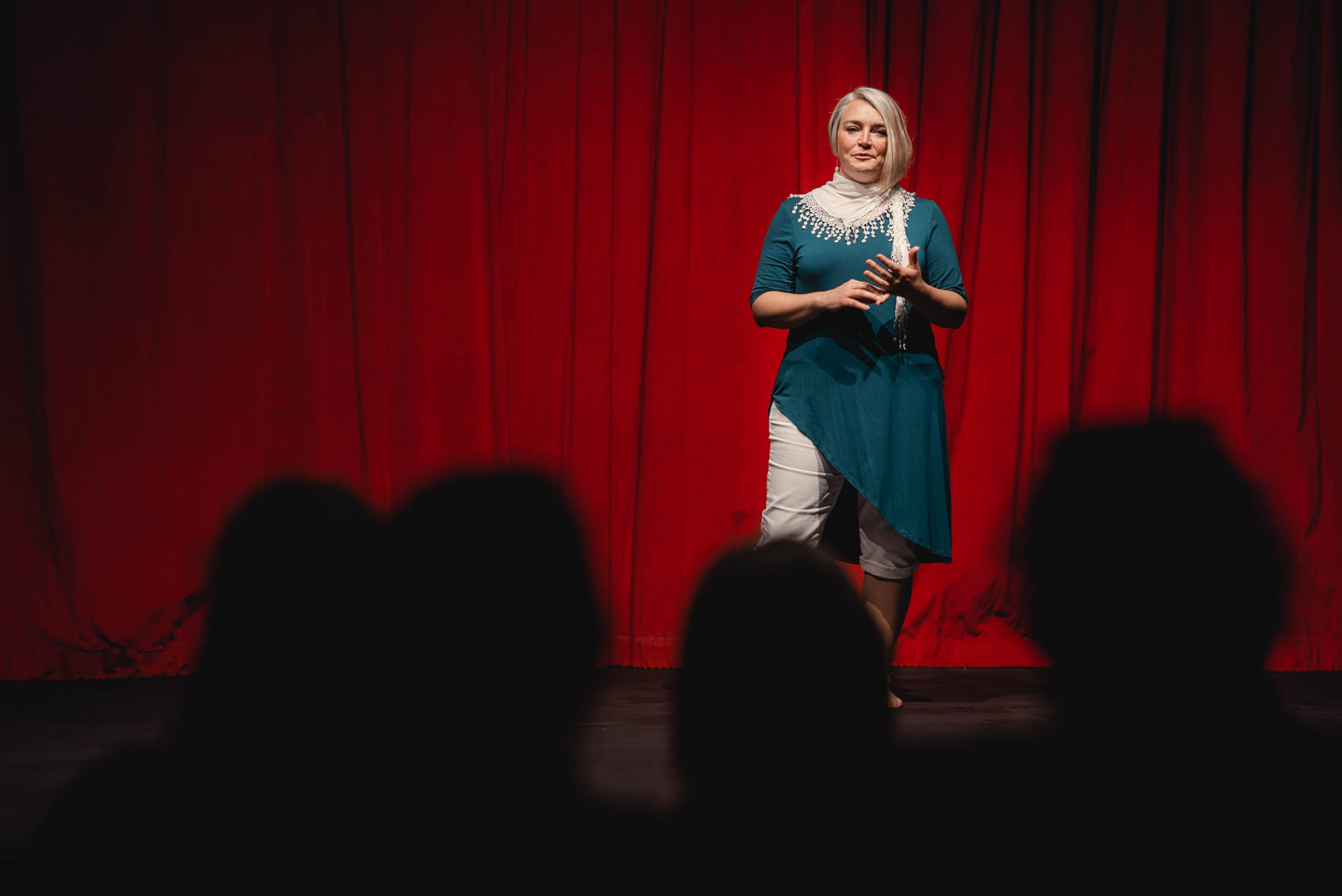 Krystal Jakosky in teal shirt on stage with red curtain