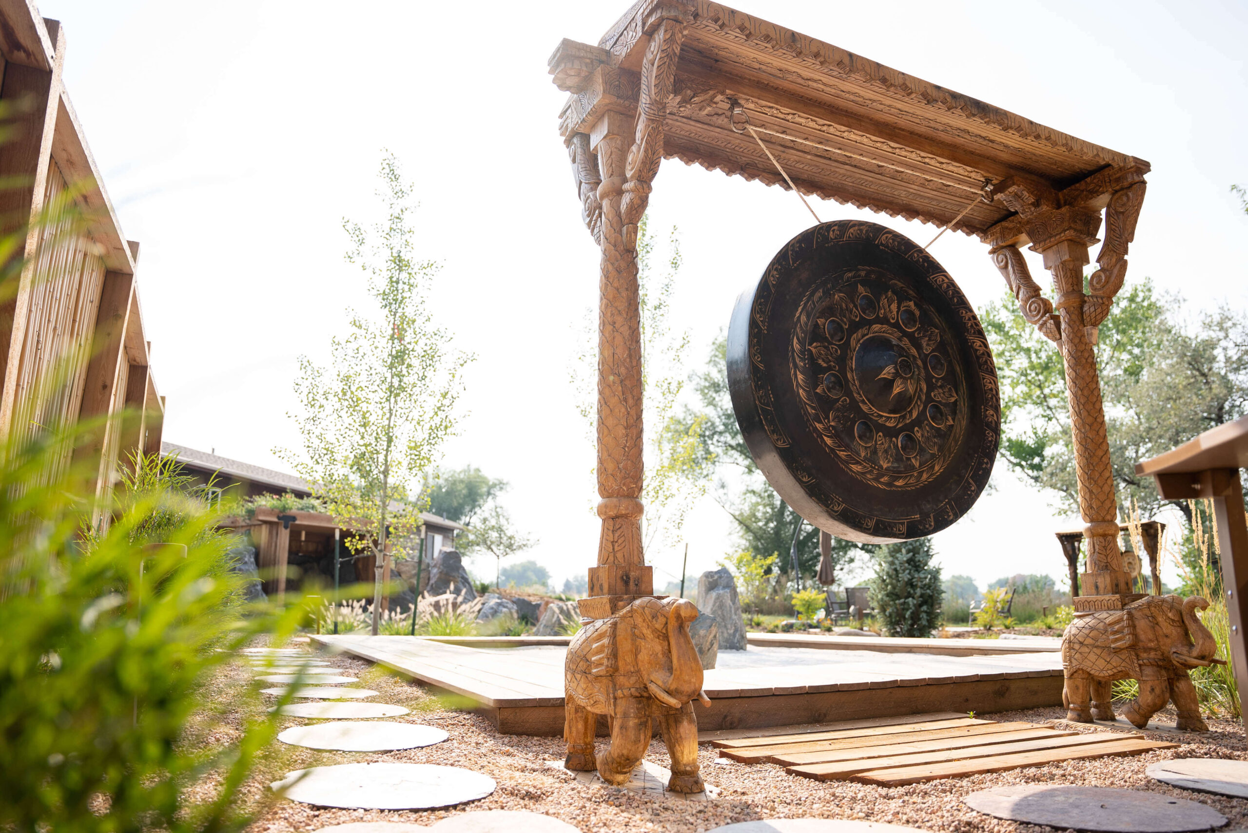 Explore the Gardens at The Beam and Bell Large gong hanging from wood elephant frame in front of zen garden