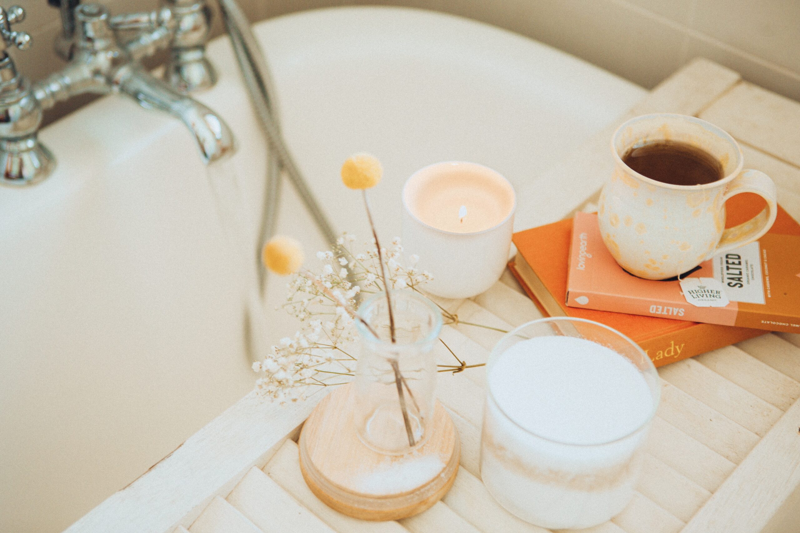 38: How to *Actually* Achieve Your New Year's Resolutions a white bathtub with a tray over it containing flowers, a candle, books, and a cup of coffee