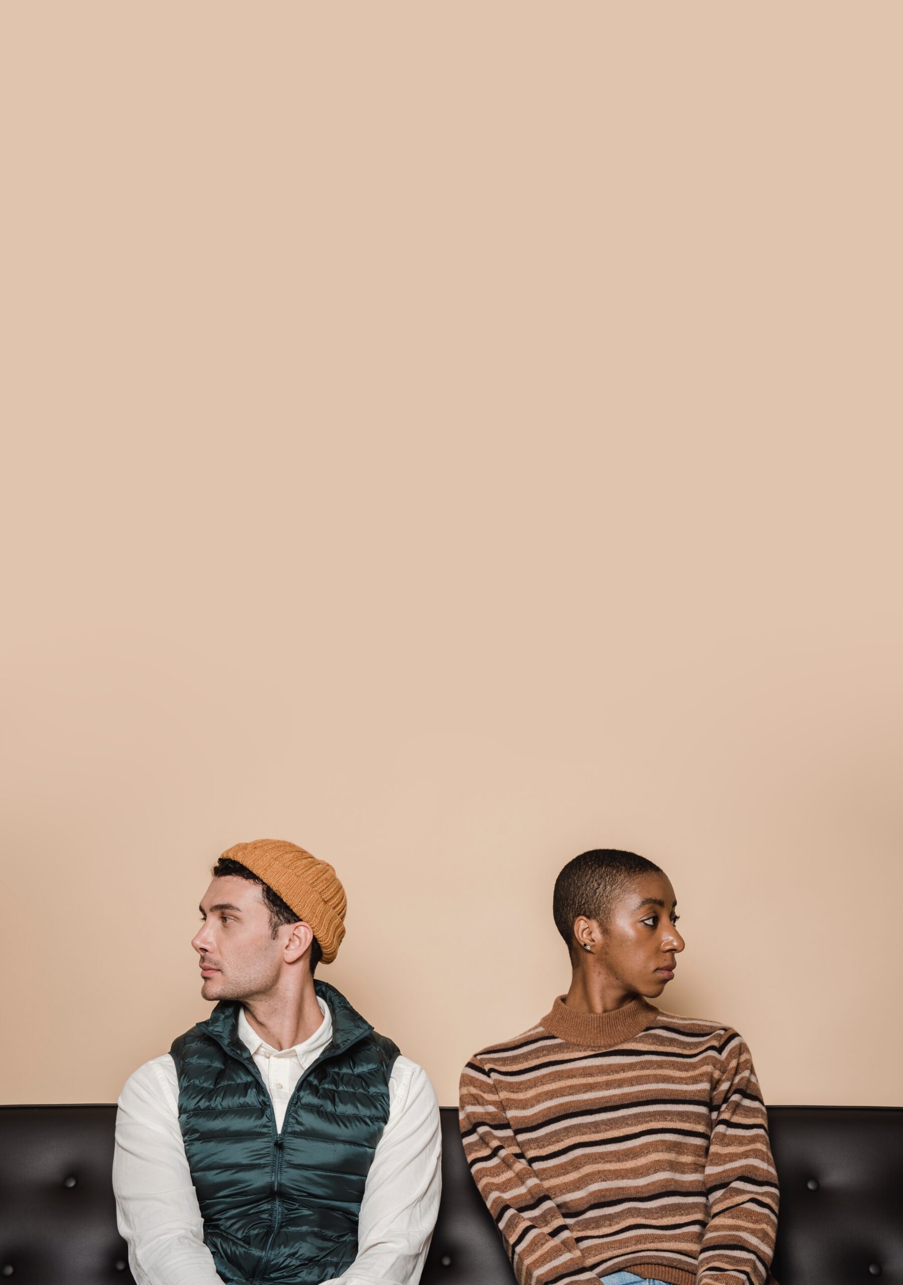 a man and a woman sitting against a tan wall looking away from each other