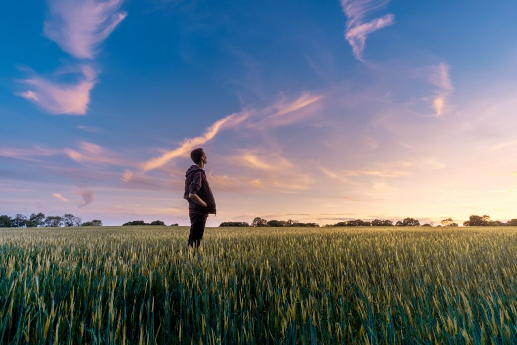 a man standing with his hands in his pockets in a green field at sunset