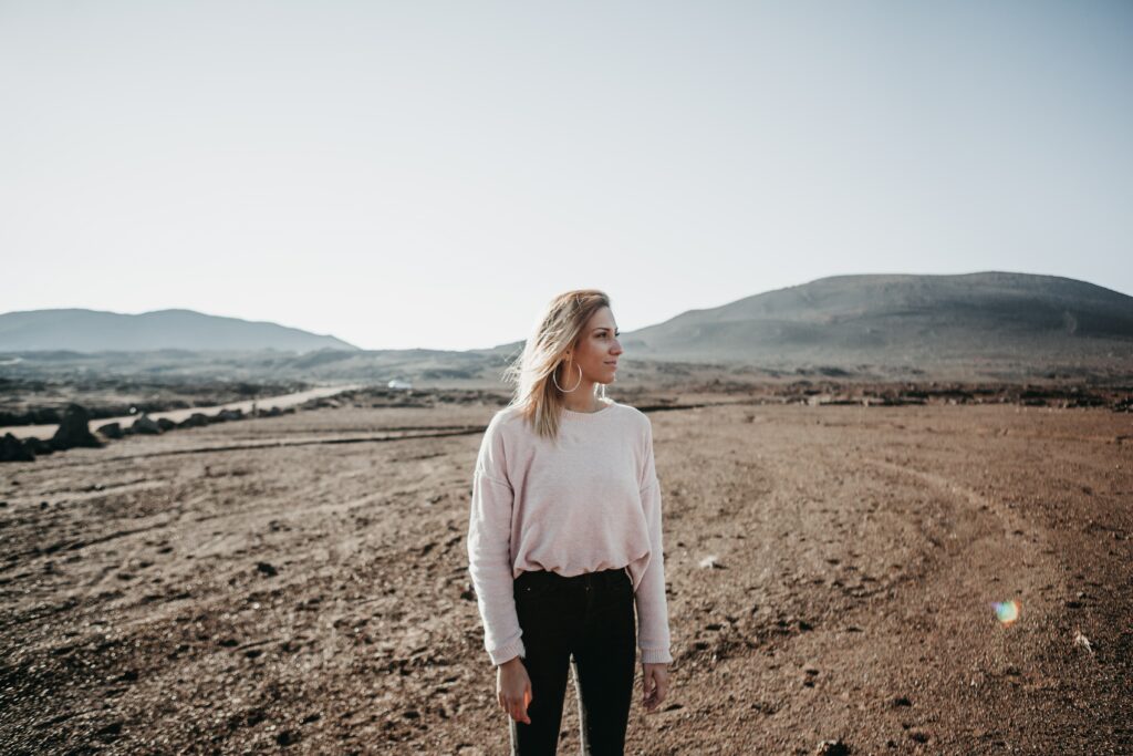 a woman in a pink sweatshirt in a desert with mountains in the background