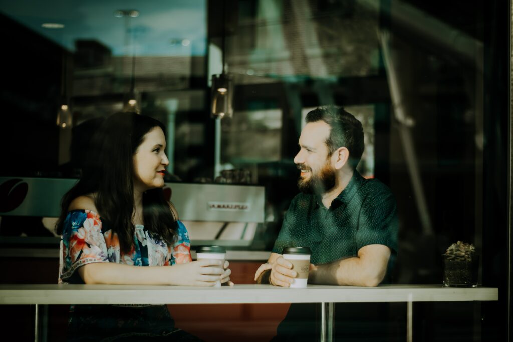 a man and a woman sitting by a window of a cafe talking and smiling