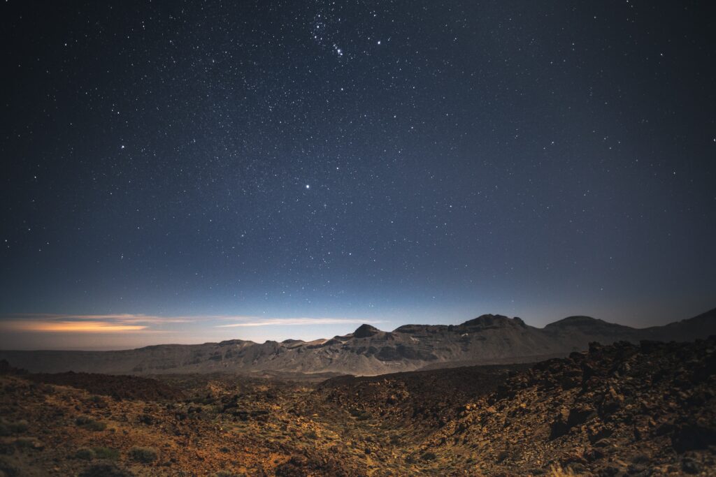 mountains in the desert with a dark sky and thousands of stars