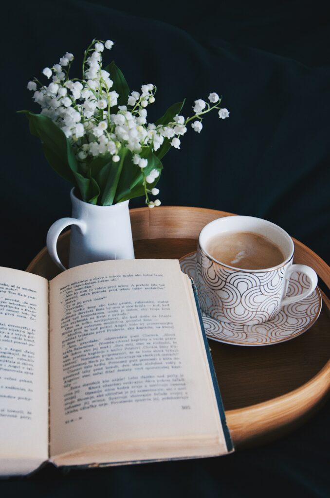 open book on a wooden table with a cup of tea and white flowers