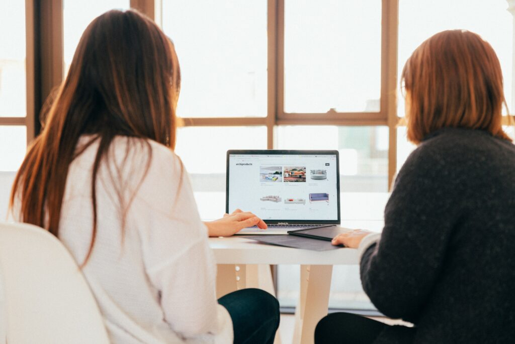 two women sitting at a white table looking at a laptop