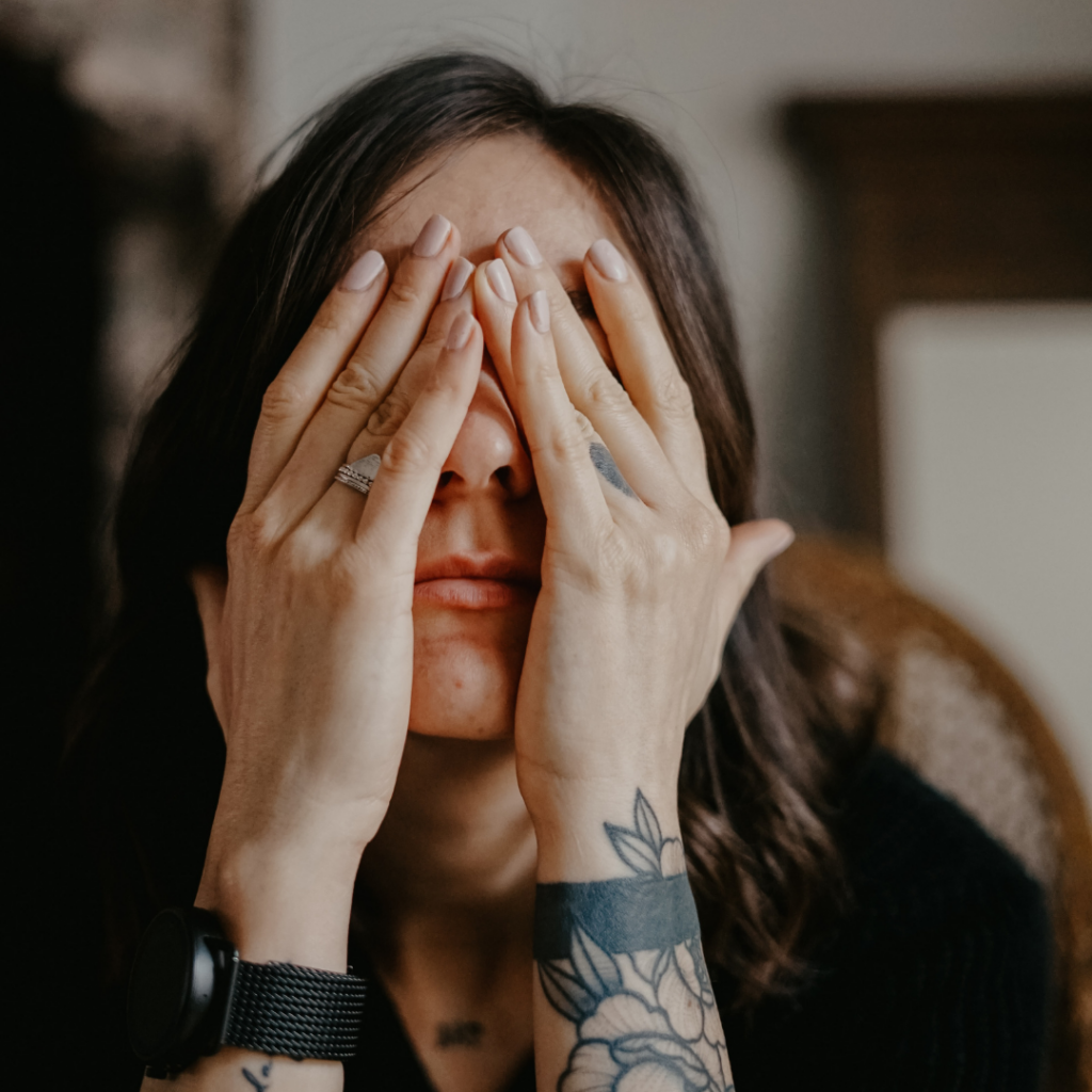 close up of a woman with tattoos with her hands on her face covering her eyes