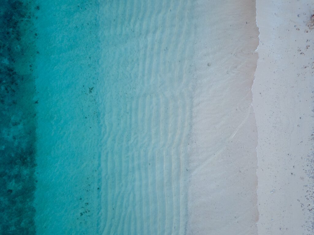 birds eye view of blue waves gently crashing onto a white sand beach